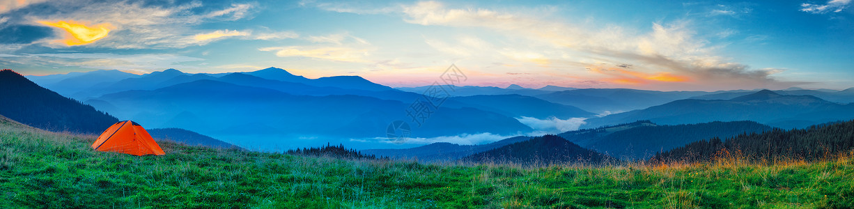 天空绿草风景山平原上的全景橙色帐篷背景图片