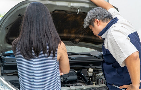 服务车辆汽机械师检查引擎以找到原因由车主站立的女士来查车库图片