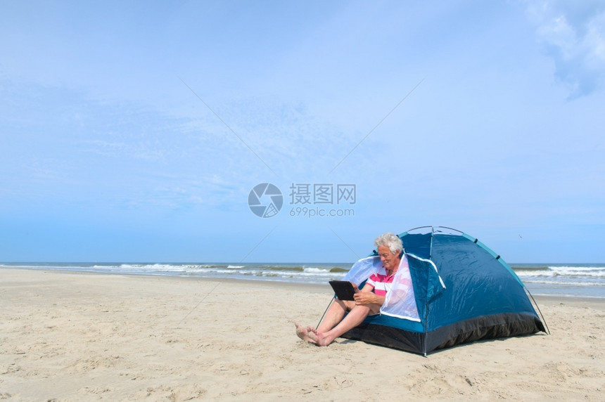 短裤单身老人在海滩的避难所内有数字石板露营网络放松图片