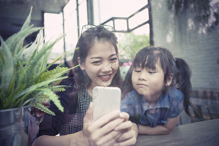 活的社会母亲正在家中客厅寻找智能电话屏幕的年青亚洲小妇幼女和儿童图片