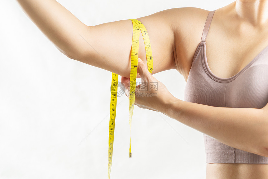 不开心身体女人用测量胶带捏着她过度脂肪的手臂妇女饮食生活方式的概念注重量图片