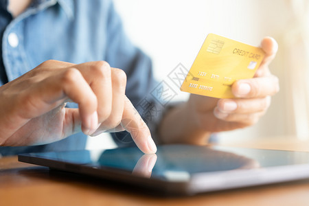 手托平板电脑正在做随意的卡片利用平板电脑和进行网上交易的男子在使用平板电脑并进行在线交易网上购买信用卡背景