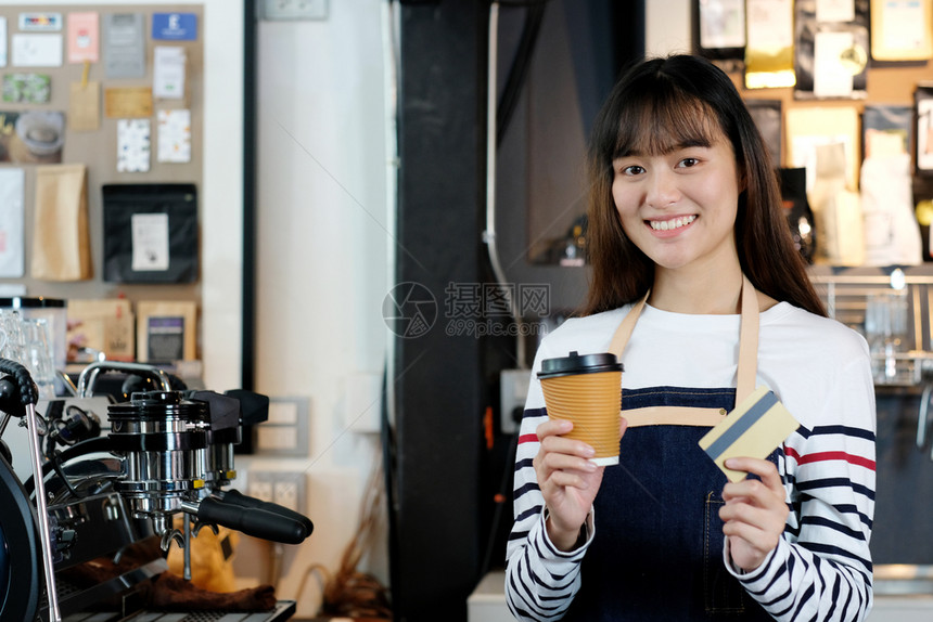 保持在咖啡馆柜台背景小商业主食品和饮料业概念上面笑脸持有可支配咖啡杯和信用卡的年轻女青律师协会手金融图片