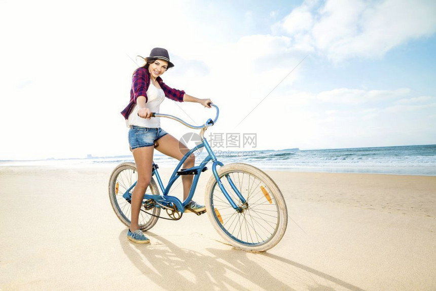 帽子自然一个有魅力的年轻女子在海滩上骑着自行车假期图片