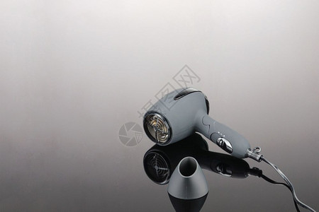 电动吹风机造型关心专业的灰色镜面背景上用于美发沙龙或理店的灰色垫子电动手持式吹风机灰色镜面背景上的灰色垫子吹风机背景