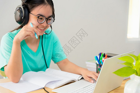 带眼镜戴耳机的亚洲年轻女学生在笔记本电脑上愉快地在线学习图片