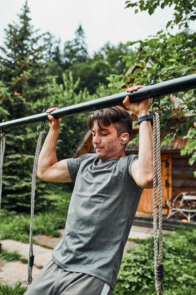积极的运动员年轻人在暑假期间露营时进行体操锻炼在引向上单杠做引体向叉图片