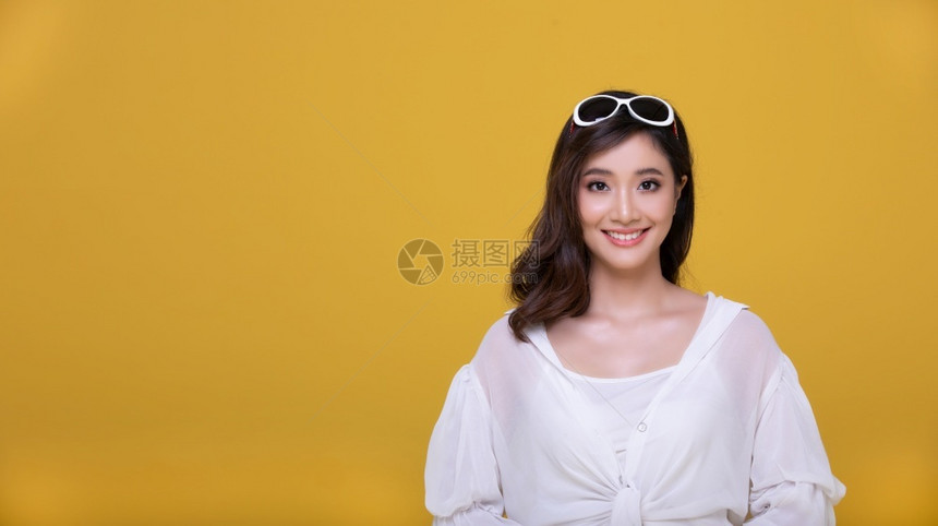 白种人闲暇亚洲美丽的快乐年轻女带着阳光眼镜笑欢看在黄色工作室背景上被孤立的相机人们图片