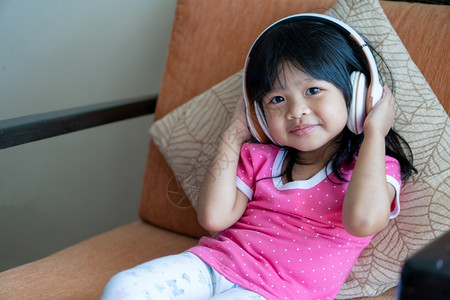 技术手机无线的快乐亚洲女孩微笑并享受在沙发客厅用耳机收听音乐可爱的高清图片素材