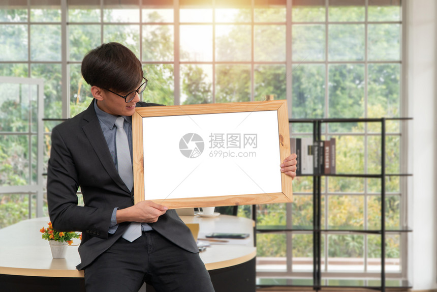 拥有空白板坐在办公室桌上边的亚洲快乐青年商人对广告文本和内容复制空间概念的构思广告文字和内容的复制空间抓住介绍套装图片