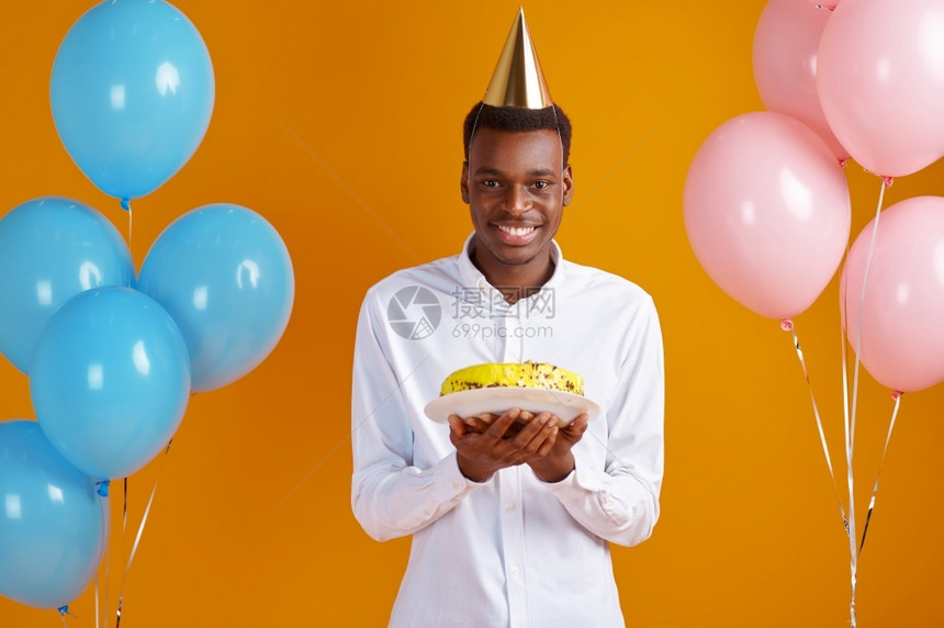 焰火带着生日蛋糕黄色背景微笑的男得到一个惊喜庆祝活动气球装饰和生日蛋糕的盖子人infowhatsthis拿到图片