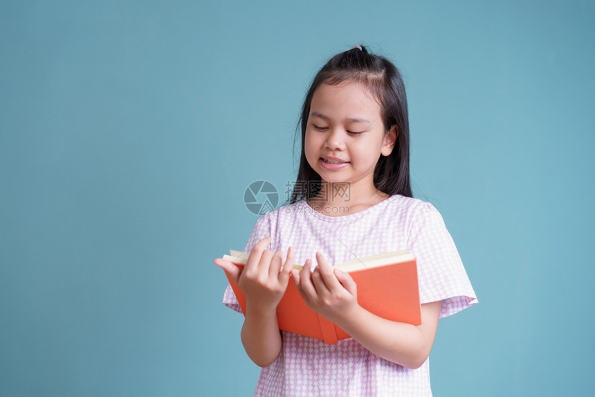 亚洲快乐的小女孩站着阅读书关于蓝背景孤立的色复制室内的在家工作图片