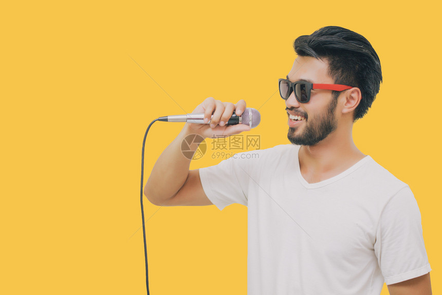 带着胡子的亚洲英俊男笑着歌唱在黄色背景下被孤立的麦克风歌手嗓音工作室图片
