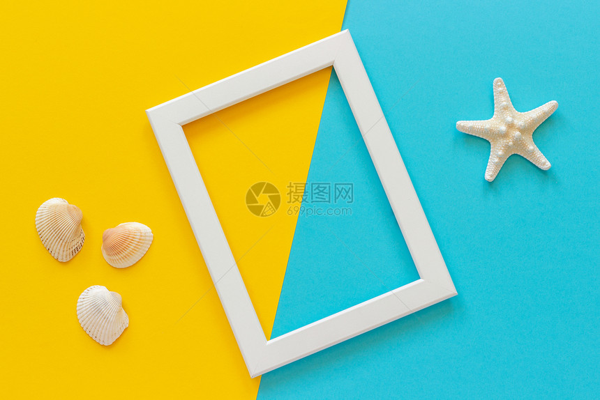 海滩蓝色黄背景和贝壳上带有海星的白框用于明信片的创意平躺顶视图模板设计用于文本的复制空间蓝色黄背景和贝壳上带有海星的白框用于明信图片