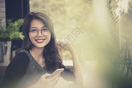 手拿着智能机的年轻亚洲妇女脸上笑着微的脸单身头发快乐聊天高清图片素材