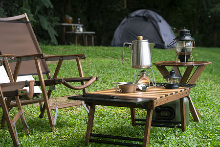 野餐露营区绿草坪上桌板的便携式燃气炉碗和灯背景图片