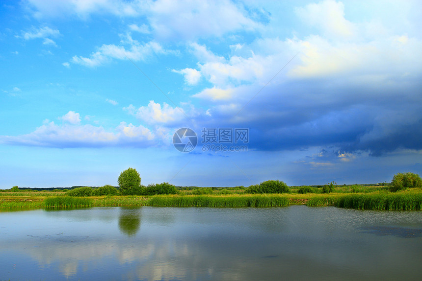 水在美丽的自然风景中奔流而出池塘和云彩湖面与甘蔗和大云环绕的湖面林木在美丽的自然景观中横冲直撞夏天芦苇图片