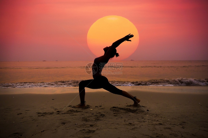 灵感的日出时在海滩上做瑜伽的年轻女子和平图片