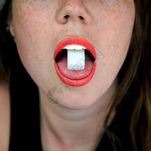 吃葡萄糖一个女人嘴里舌头上有方糖的特写不健康食物糖果甜概念饮图片