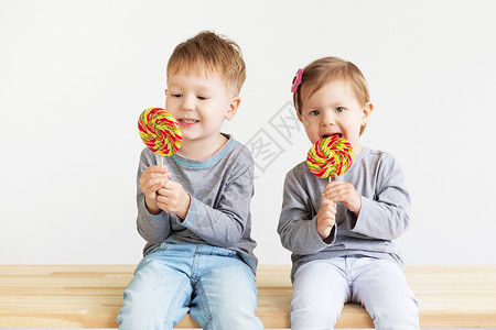可爱的坐着孩子们吃棒糖快乐的孩子带着一大颗糖果快乐的小孩子肖像一个快乐的小孩子男和女美丽的子在白色背景下愉快甜的高清图片素材