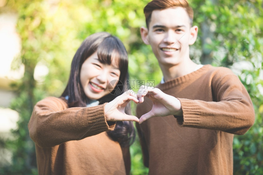 男朋友随意的美丽年轻夫妇用手创造心形在户外的爱中快乐地微笑浪漫图片
