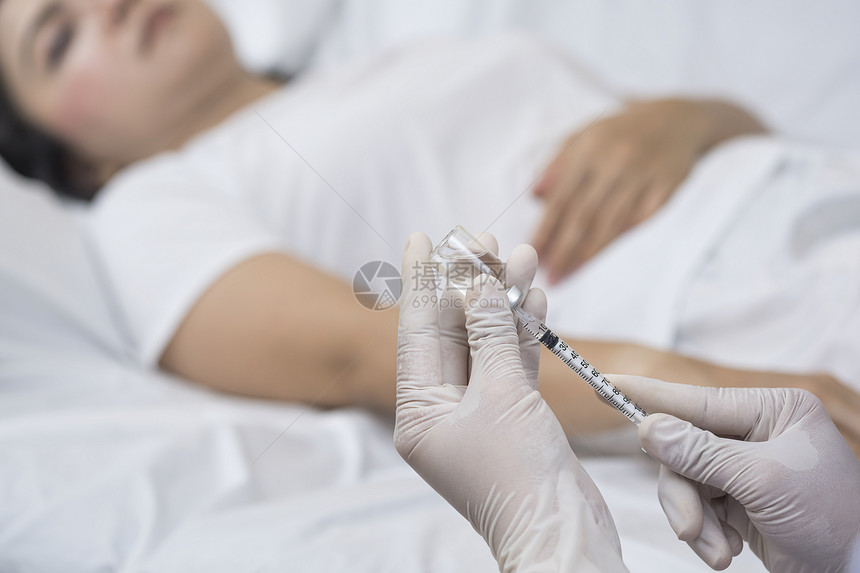白色的泰国女士集中关注医生手持的抽用注射针筒和小瓶以便注射给在医院病房床上的女人图片