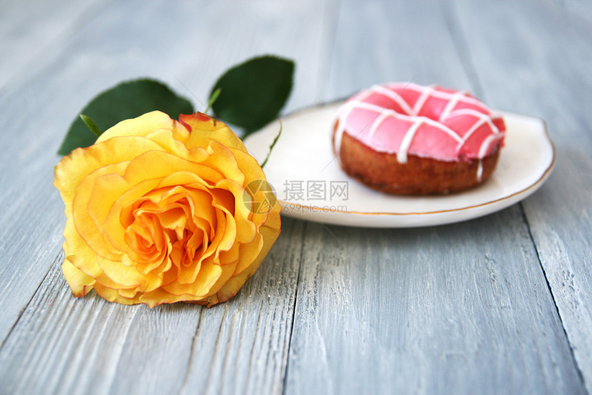 一朵美丽的黄玫瑰有开着的芽和甜圈白陶瓷板上有粉红冰淇淋灰色木质背景空间自然卡片爱图片