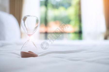 清晨阳光下躺在床上的沙漏流经玻璃灯泡测量穿越时间倒计最后期限生命和退休日常概念等情况窗户滴漏专业的背景图片