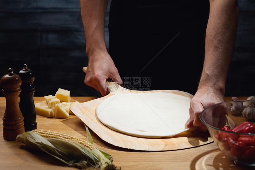 手工制作的厨师做比萨饼在低键镜头上放空披萨底盘手紧桌上有些原料生的图片