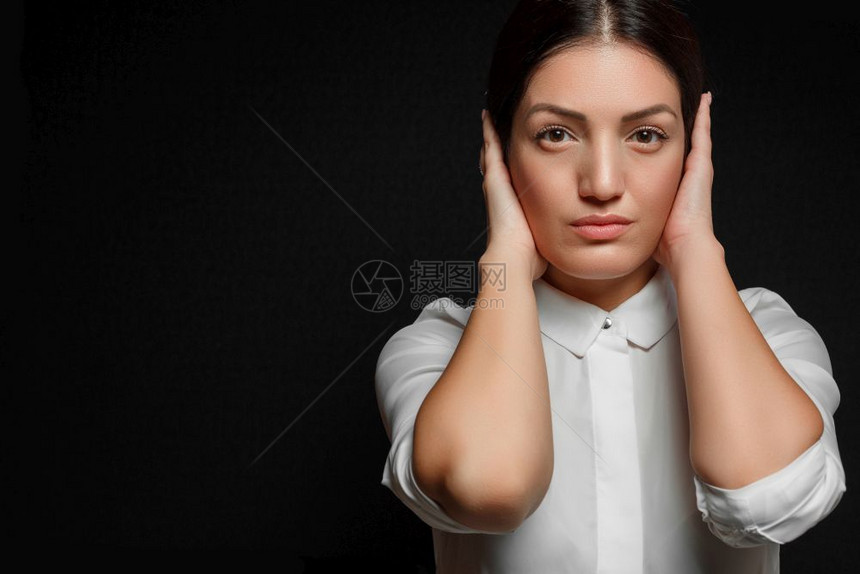 黑色的一个亚洲发女人的肖像身着白衬衫她的脸和耳朵被蒙上用她的手在黑色背景上嘴伤心图片