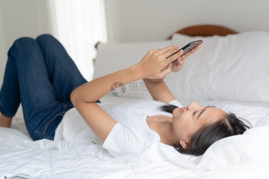 互联网成人美丽的亚洲年轻女正在使用智能手机与朋友聊天在家中的床上打着视频电话和请享用图片