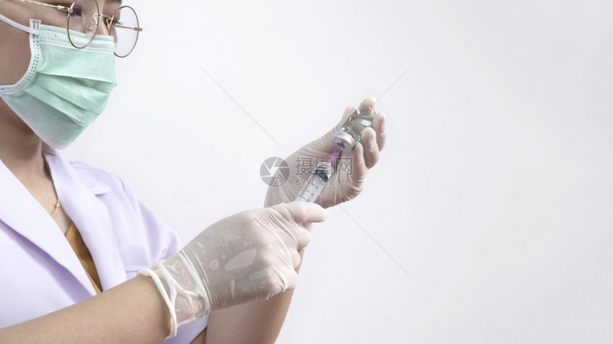 穿新冠女医生佩戴防护面具和医疗手套并携带注射器和药瓶准备在白色医院房间背景下注射防伤药品图片