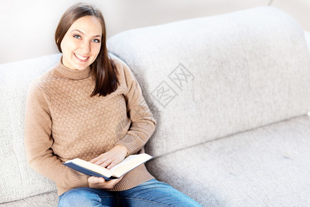 房间照片坐在沙发上随便微笑的女人与一本书起坐在沙发上放松阅读图片