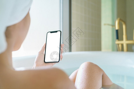 干净的浴室女用手机空白屏幕显示清晨用智能手机在浴缸里放松展示图片