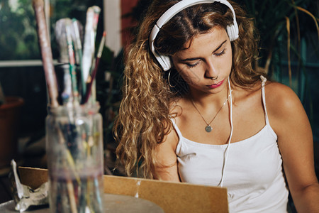 帆布灵感职业在工厂作室的画布上涂有耳机的女专业艺术家室内拍摄手持耳机的刷子高清图片素材