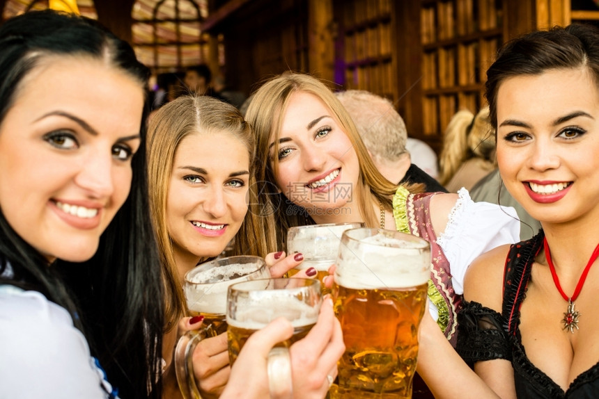 穿着传统Dirndl服装的女孩在Oktoberfest喝啤酒和玩乐混杂种族1个亚洲人俄罗斯2高加索女孩团体餐厅庆祝图片
