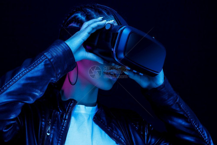 快乐的黑色身着眼镜非裔美国年轻女子观看360度视频其虚拟现实头盔在亮光中的黑色背景上被隔离注女士图片