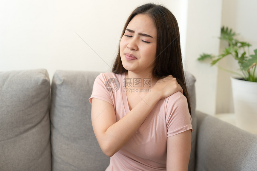 按摩亚洲女孩在家中沙发上坐时肩部疼痛年轻女孩因肌肉健康和疾病概念而痛苦坐着哭图片