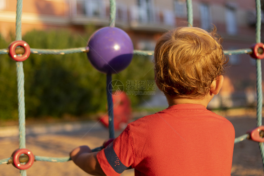 孩子们红色的金一个小男孩在日落时爬过一个儿童运动场的网图片