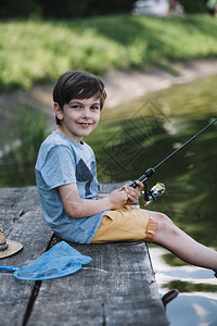 爱钓鱼快乐的男孩坐在木头码湖边拿着渔棍秋天图片