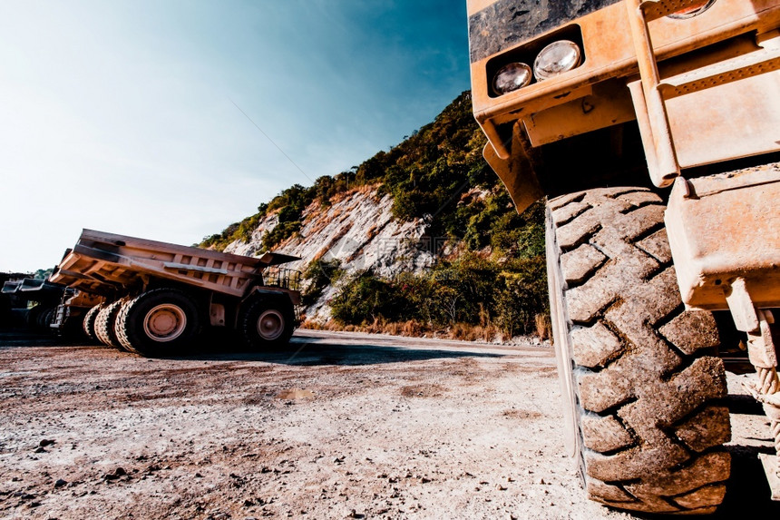 在山区附近的一个露天坑许多停在背景的大型采矿倾卸卡车上关闭大轮子运输概念是关注车轮和人们机器行业图片