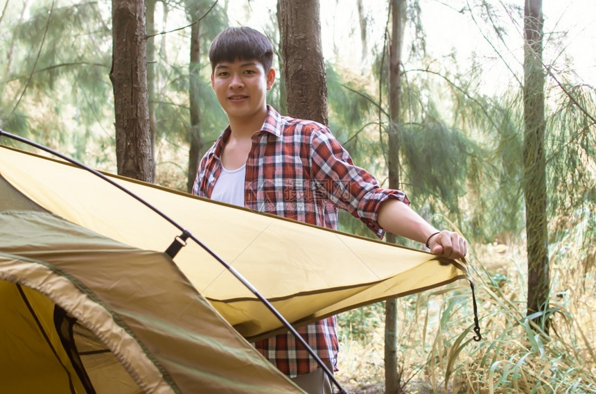 户外亚洲英俊男子在夏假露营时身穿支票衬衫和铺设帐篷的亚洲英俊男子夏季时间在森林露营远足山图片
