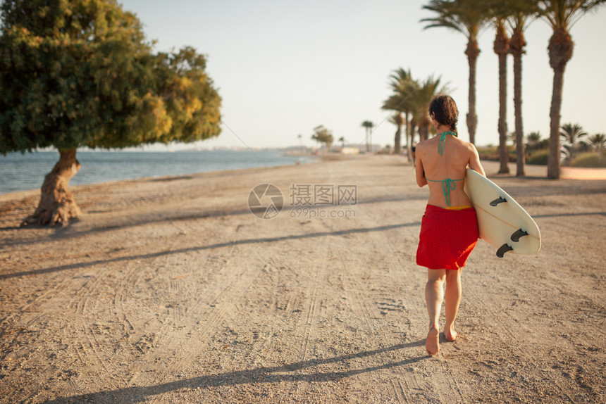 年轻女带着冲浪板在海滩上行走图片