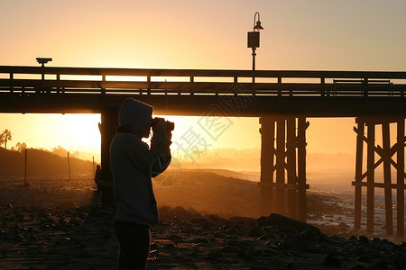 专业的橙日落时摄影师在海滩和边码头附近的日出黄昏图片