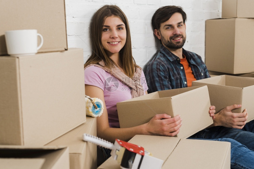 在室内真实的微笑年轻夫妇拿着纸板盒在放松新房子盒图片