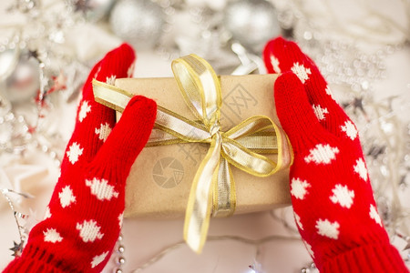 连指手套展示帽女拿着带有红色套金丝带的圣诞礼物新年心情为庆祝做准备女手拿着带有红色套金丝带的圣诞礼物为庆祝活动做准备图片