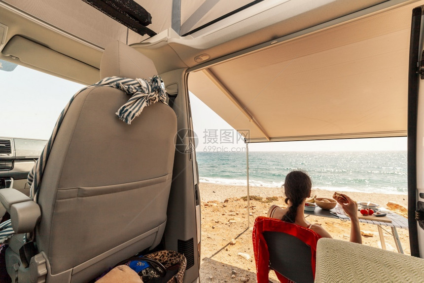 一位年轻女子在她的大篷车里吃早餐观察海滩的美景观营蓝色的图片