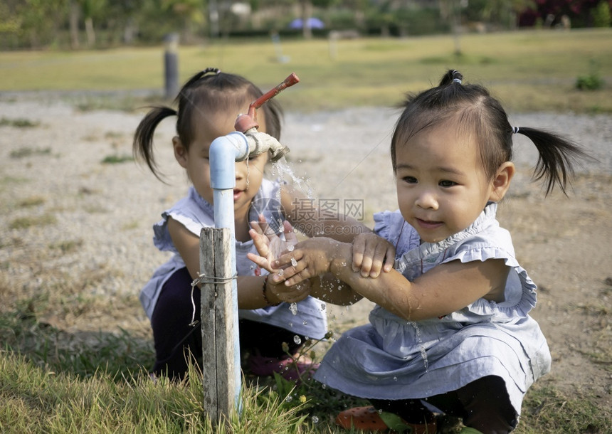 亚洲小女孩和妹用花园的钢水龙头洗手从花园里姐可爱的环境图片