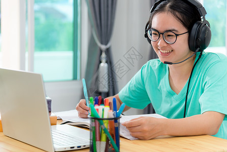 微课ppt快乐的亚洲人青年女学生带着眼镜耳机的亚洲女青年学生在一本书上寻找视频会议笔记本电脑计算机大学课程在线网上习络教育在家中学习远程教背景