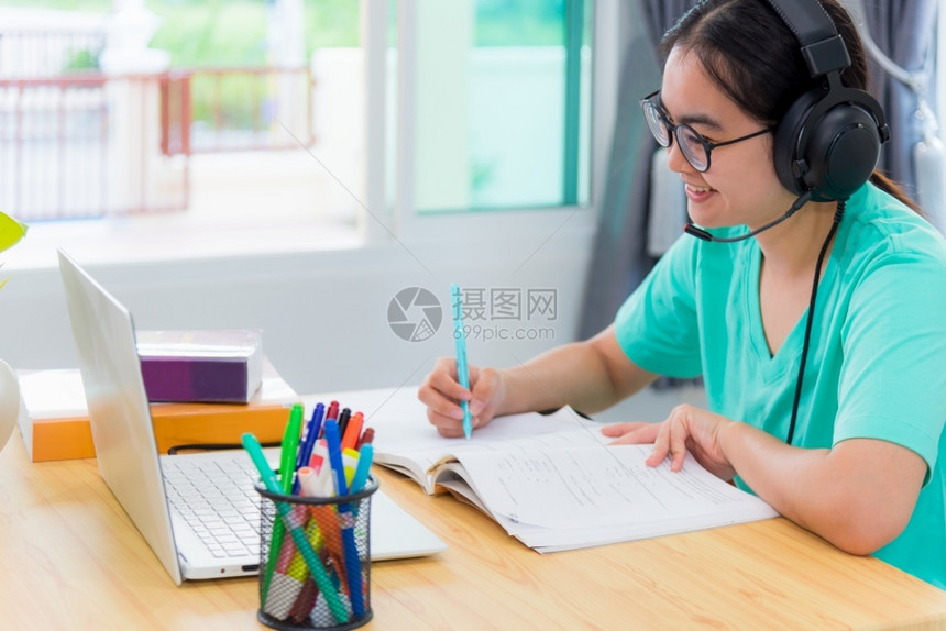 快乐的班级屋亚洲青年女学生带着眼镜耳机的亚洲女青年学生在一本书上寻找视频会议笔记本电脑计算机大学课程在线网上习络教育在家中学习远图片